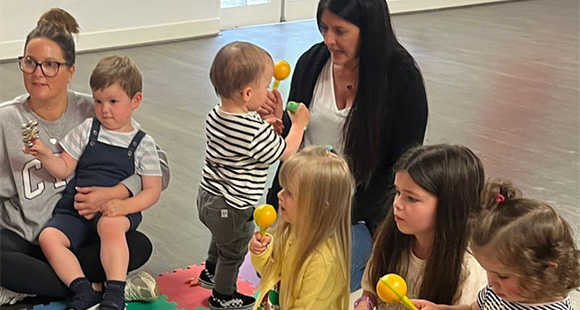 two adults with a group of five children sitting on a matt for a sensory storytelling birthday party