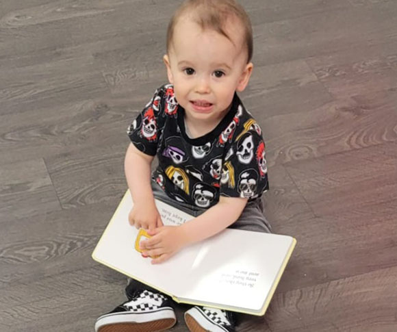 a toddler wearing a pirate shirt looking up at the camera while holding a book