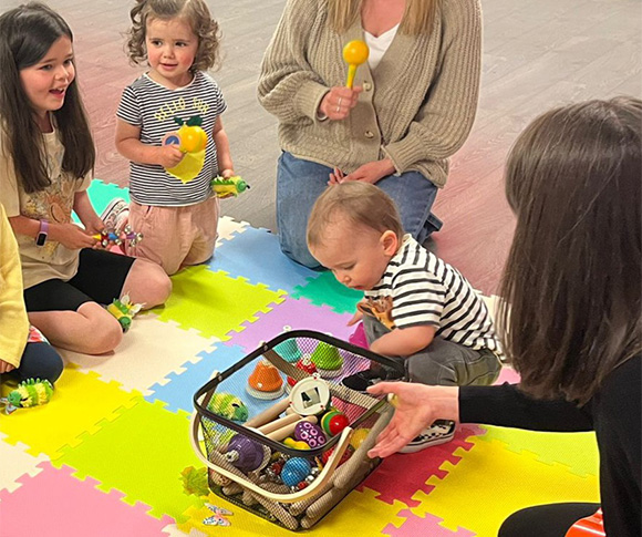 a group of children in a circle together on a matt looking at toys used to stimulate the sense of sound