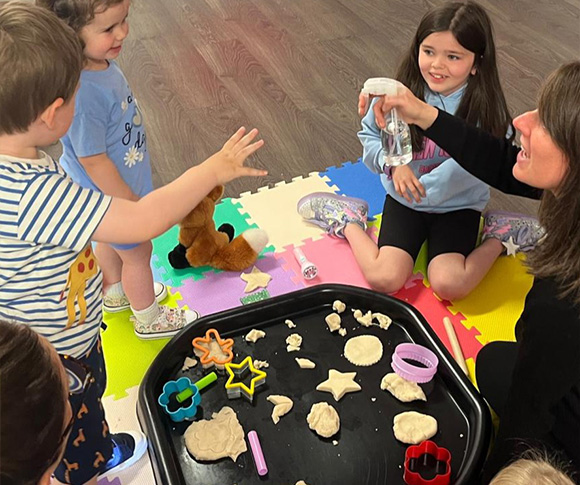 a group of children gathered around a black grey of play dough and cookie cutters