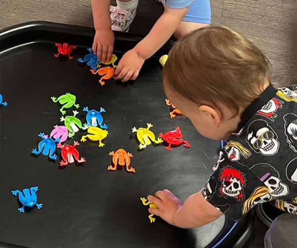 two children playing with plastic frogs in a black tray